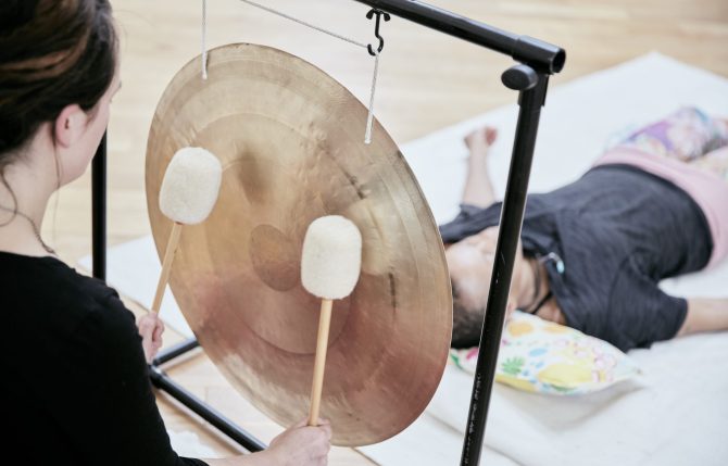 Woman striking a large gong wit soft drumsticks during a sound therapy session